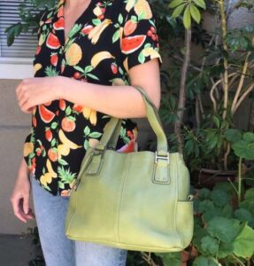 a lady with blue jeans a multicolored shirt holding olive green fossil bag 